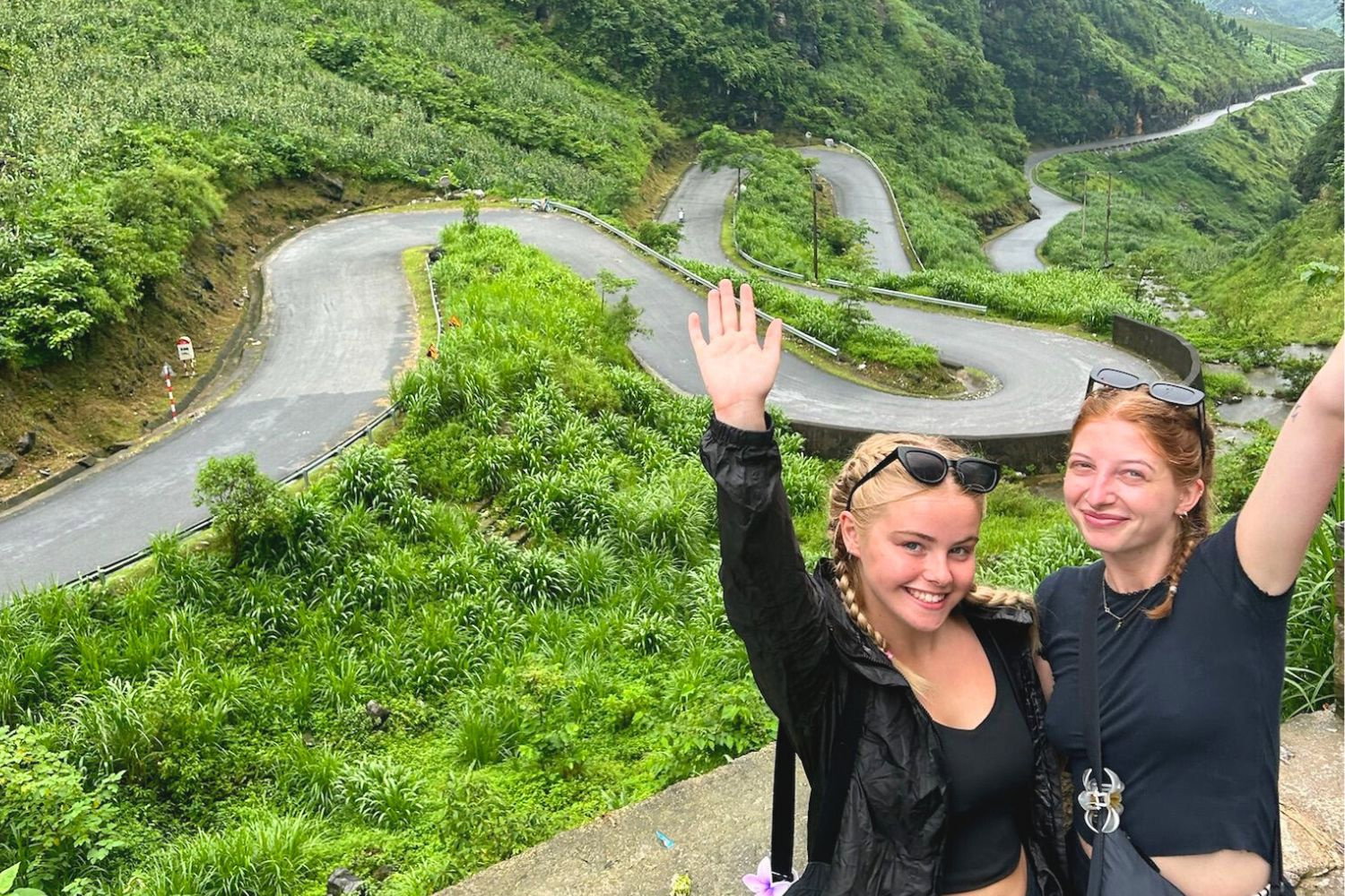Travellers with arms up by zigzag road on the Ha Giang Loop