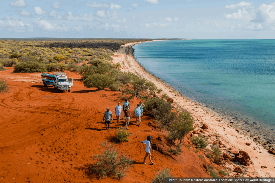 travellers walking in orange sand next to ocean