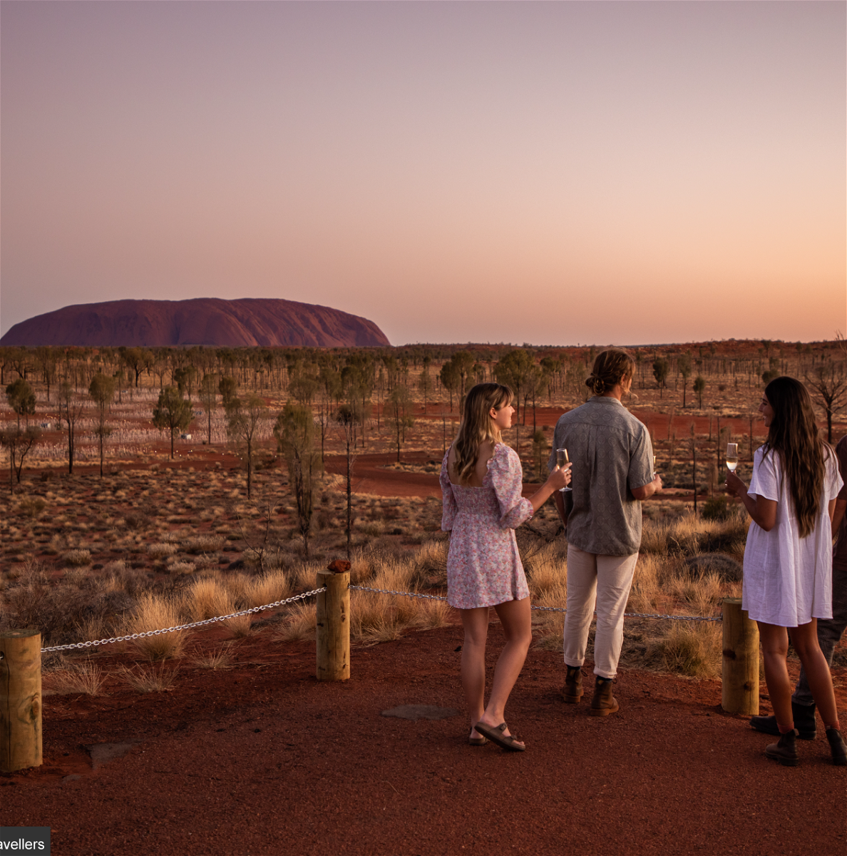 Group of travellers enjoying drink looking over uluru in Northern Territory
