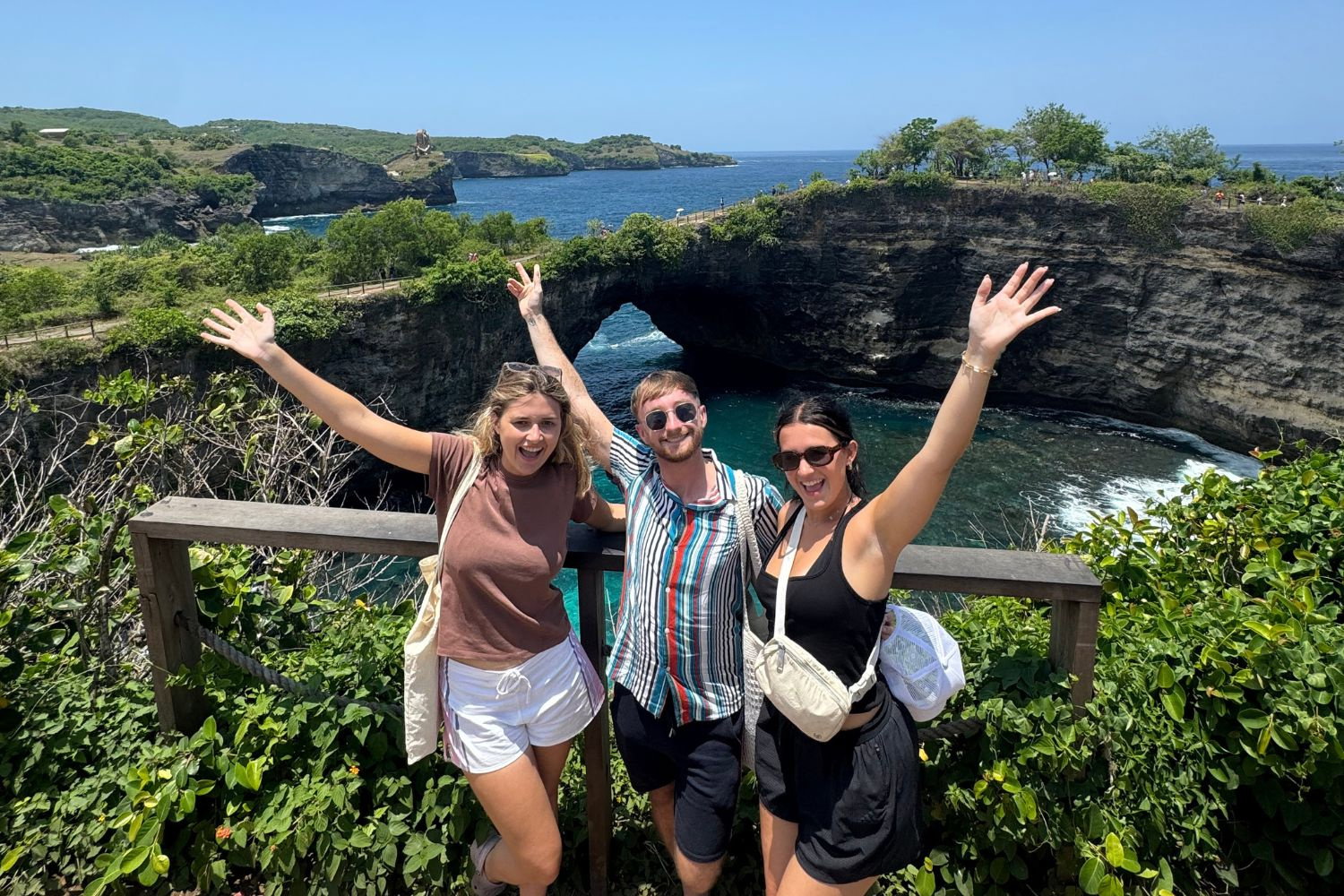 Group of travellers with arms up and smiling at viewpoint at Nusa Penida