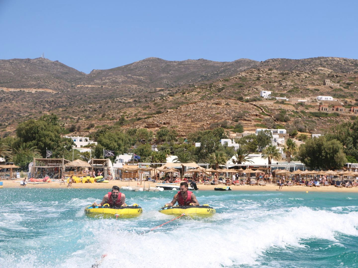 Travellers on inflatable rings in water by sandy beach in Ios