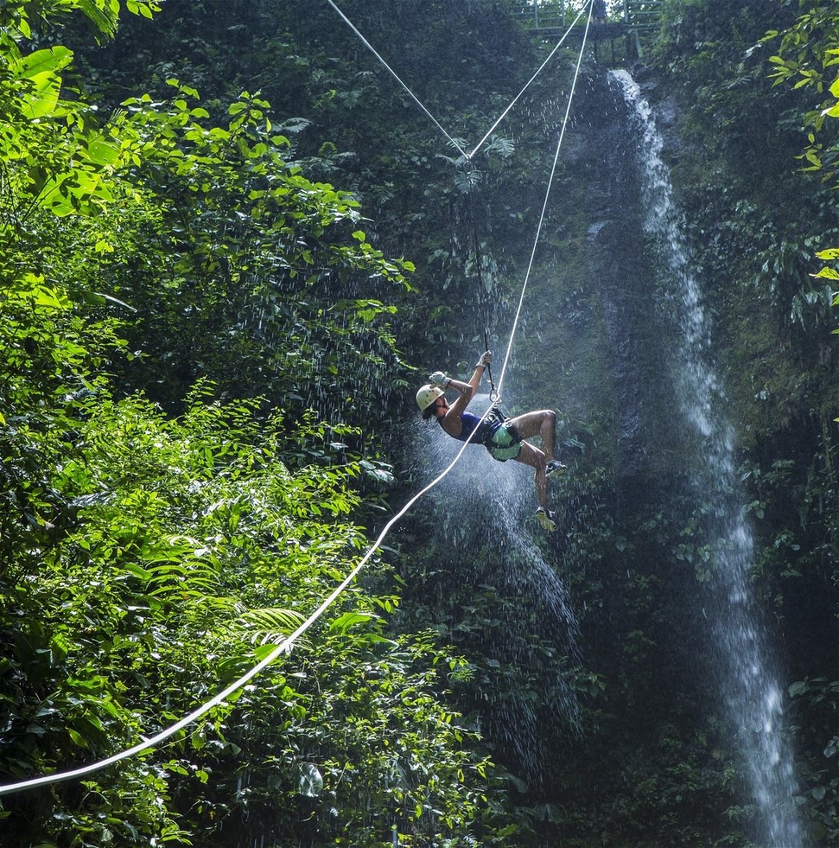 Costa Rica Adventure. person ziplining in front of waterfall in the jungle