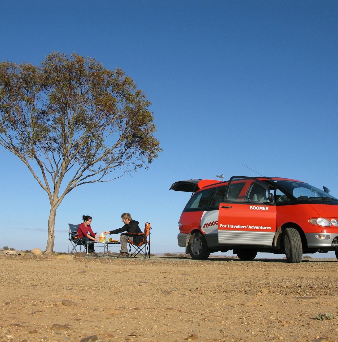 Campervan Hire Australia - red campervan with couple sitting at a table under a tree