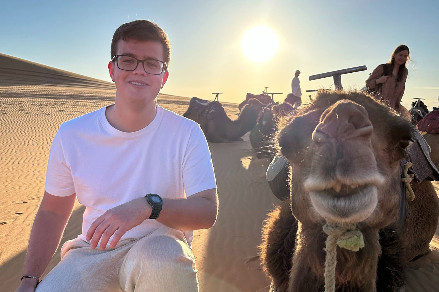 Traveller smiling beside a camel in the Moroccan desert