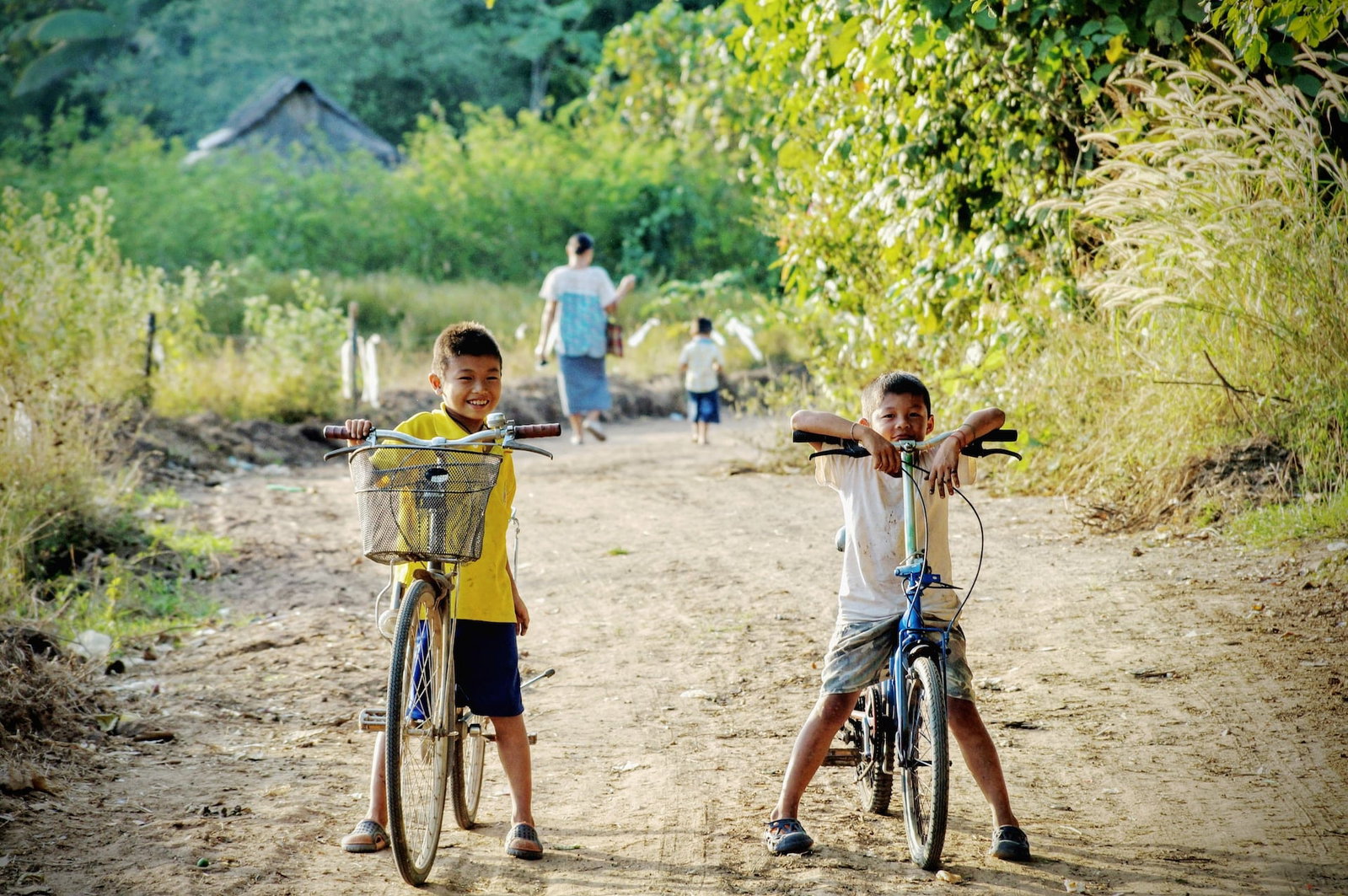 Two young Thai boys on bikes on a dirt path