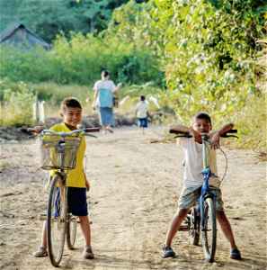 Two young Thai boys on bikes on a dirt path