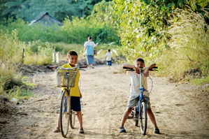 Two young Thai boys on bikes on a dirt path