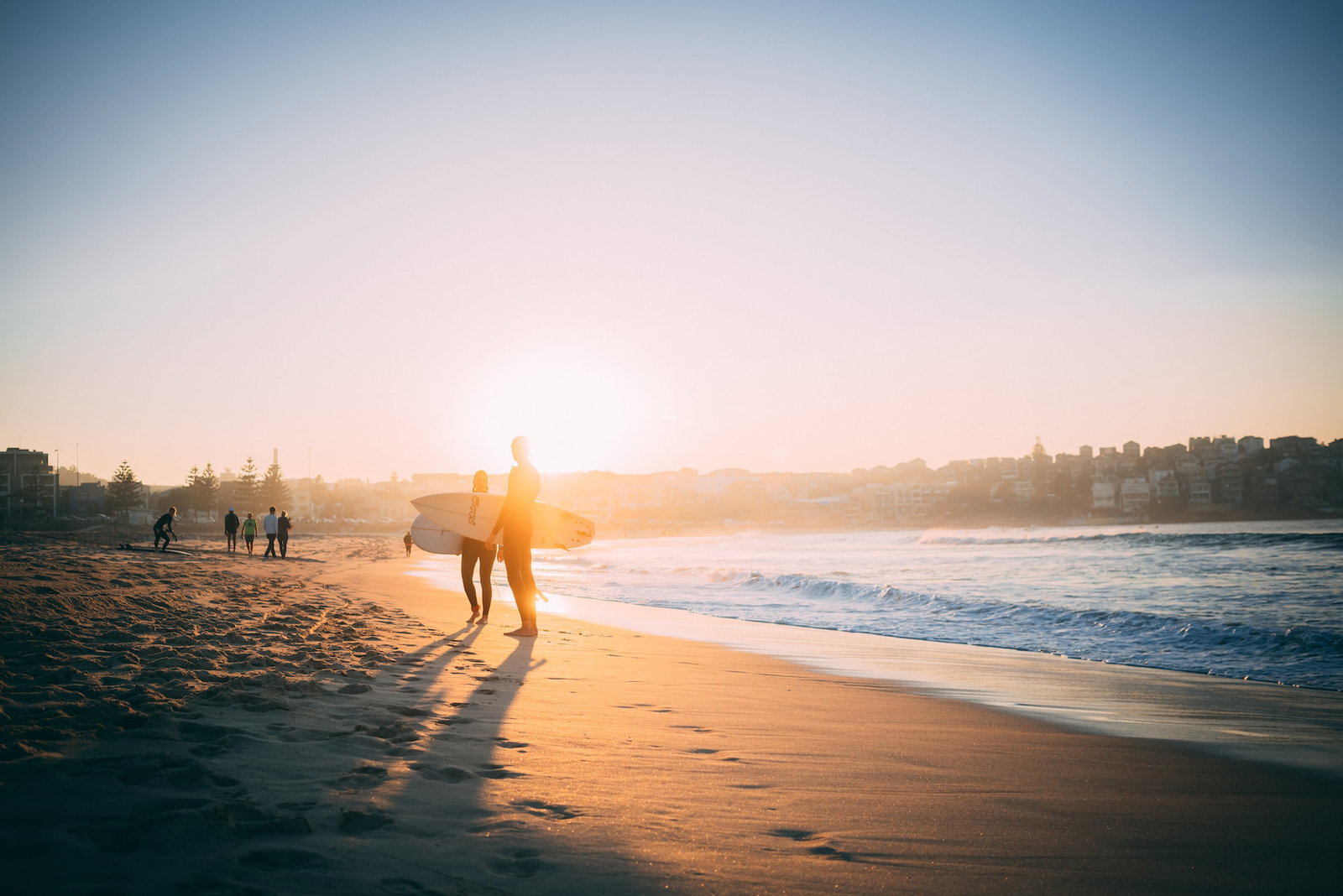 Surfers stand on the beach at sunset with surfboards in hand 