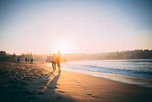 Surfers stand on the beach at sunset with surfboards in hand 