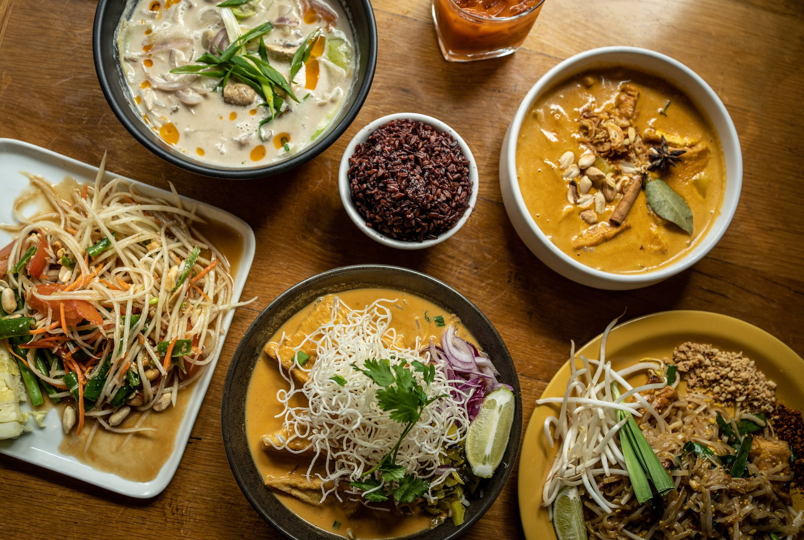 A table full of various Thai dishes, including noodle dishes and soups