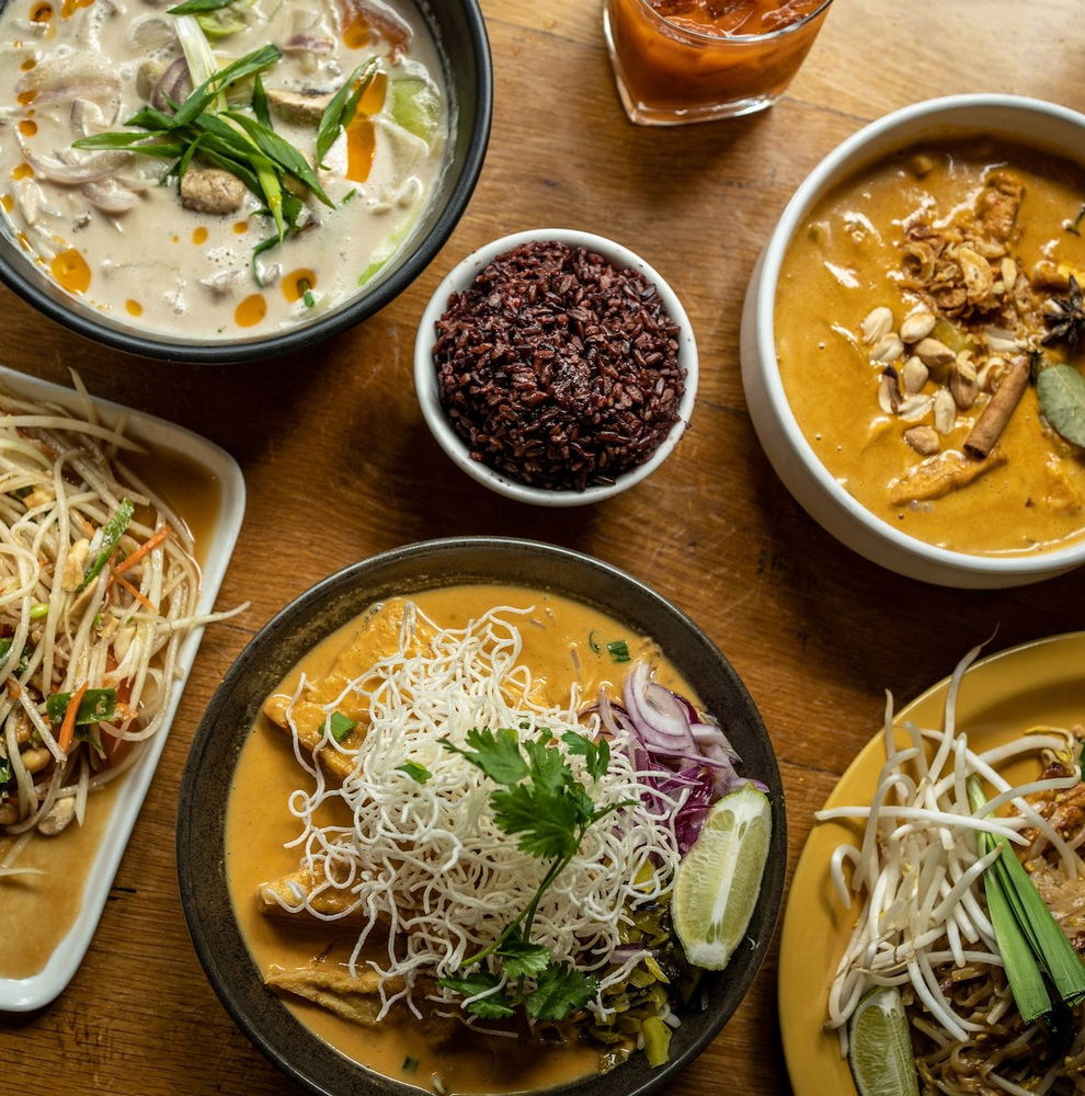 A table full of various Thai dishes, including noodle dishes and soups