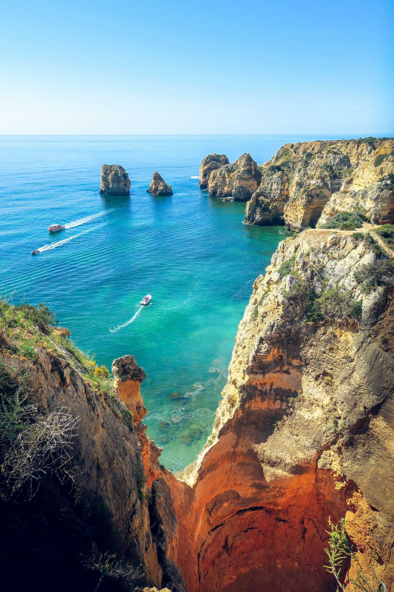 Bright blue ocean and sky with rugged cliffs and a few boats in the Algarve