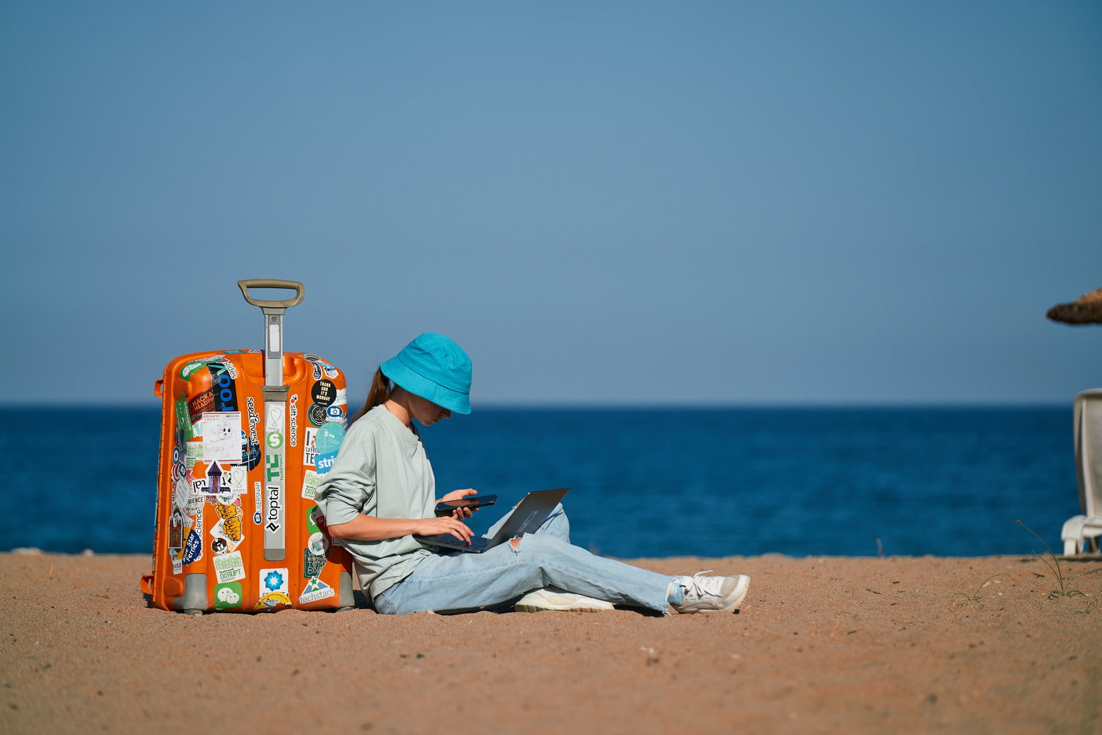 Traveller sat next to suitcase with laptop on beach
