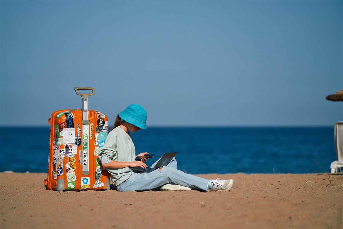 Traveller sat next to suitcase with laptop on beach