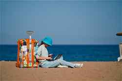 Traveller sat next to suitcase with laptop on beach