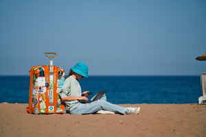 Traveller sat next to suitcase with laptop on beach