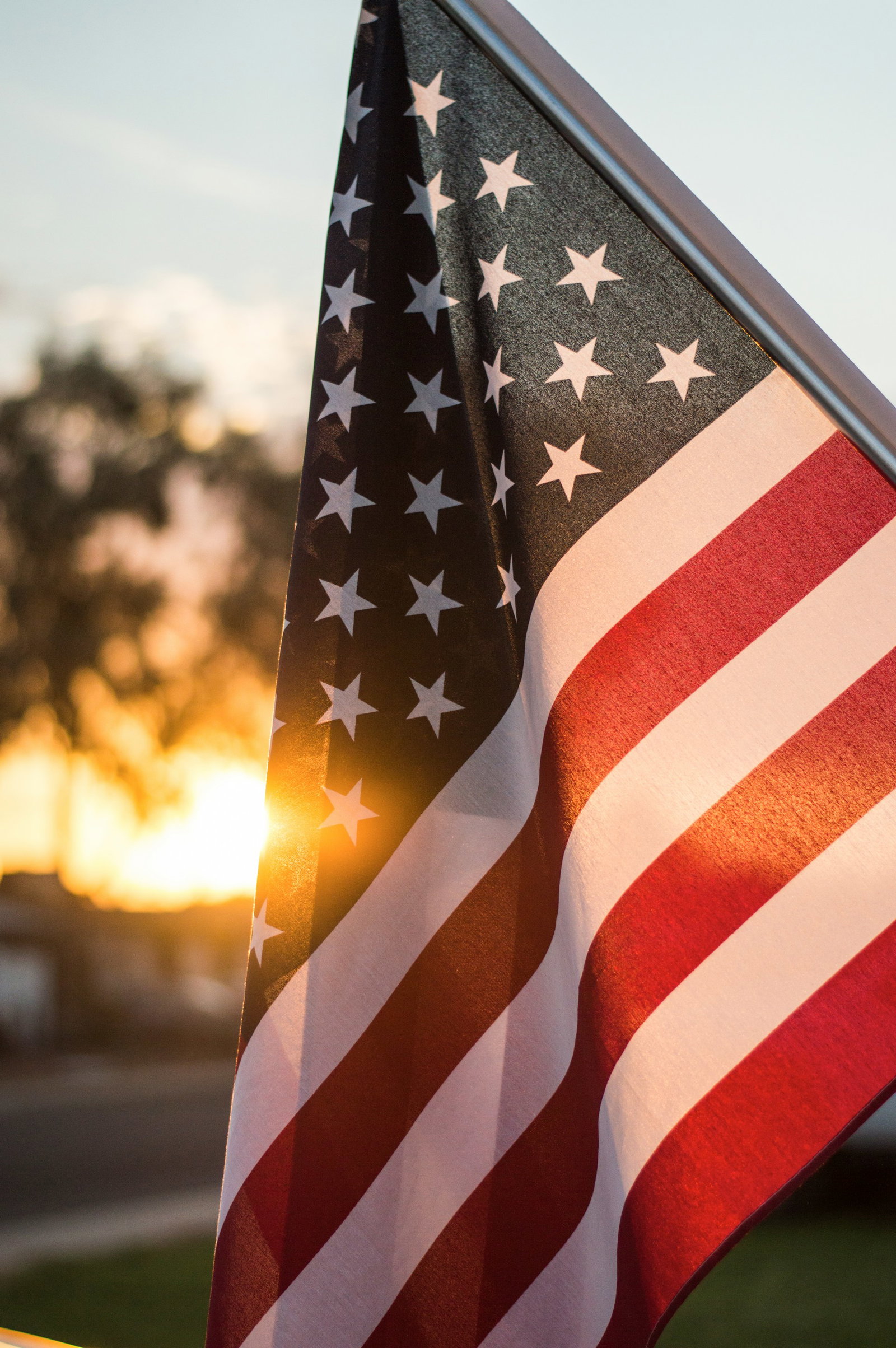 Red and white striped flag with stars in navy box up-close, golden sunlight peaking through the USA flag