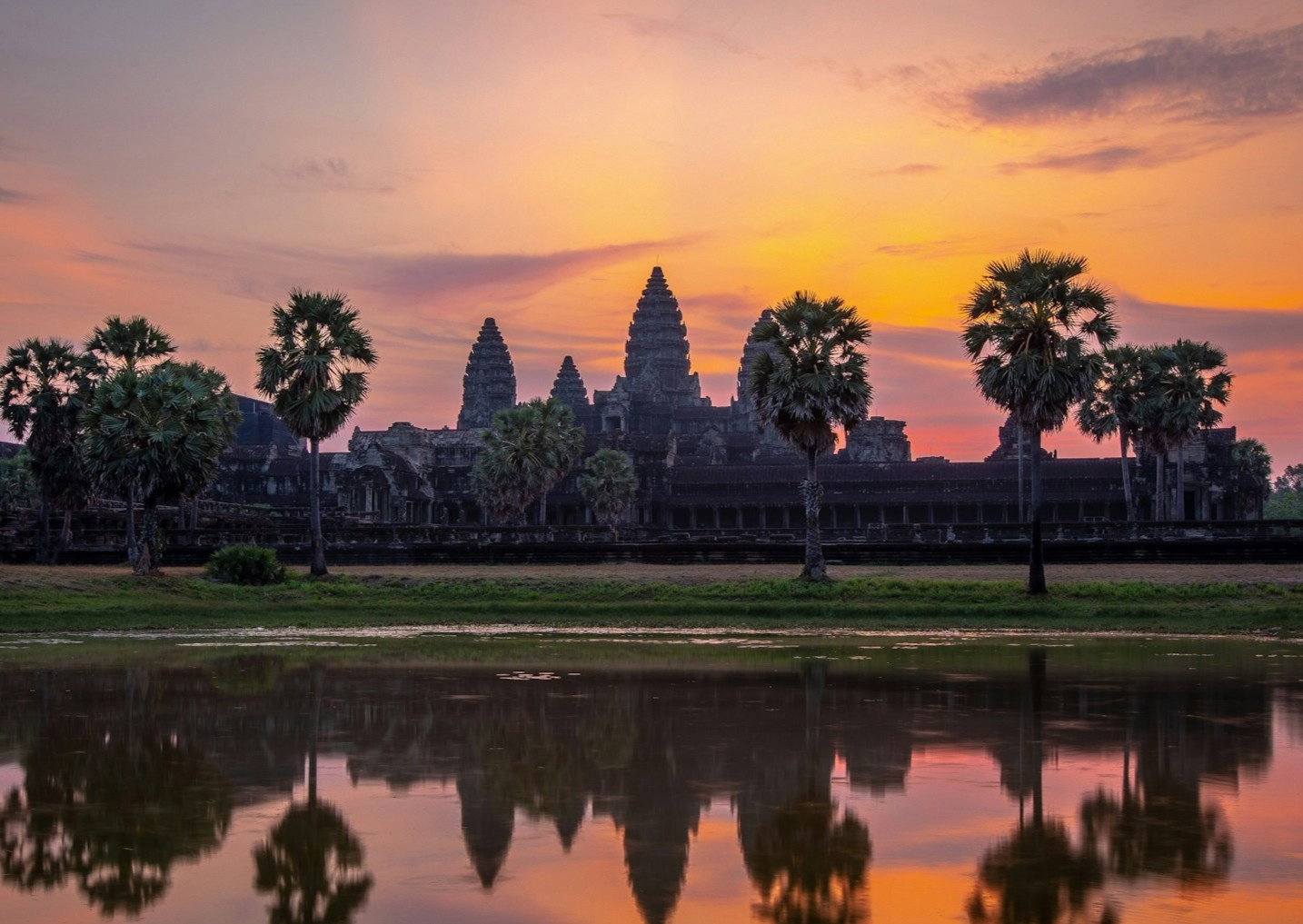 Ancient temple with lotus towers and surrounded by palm trees at sunrise with a lake reflecting the shapes and colours