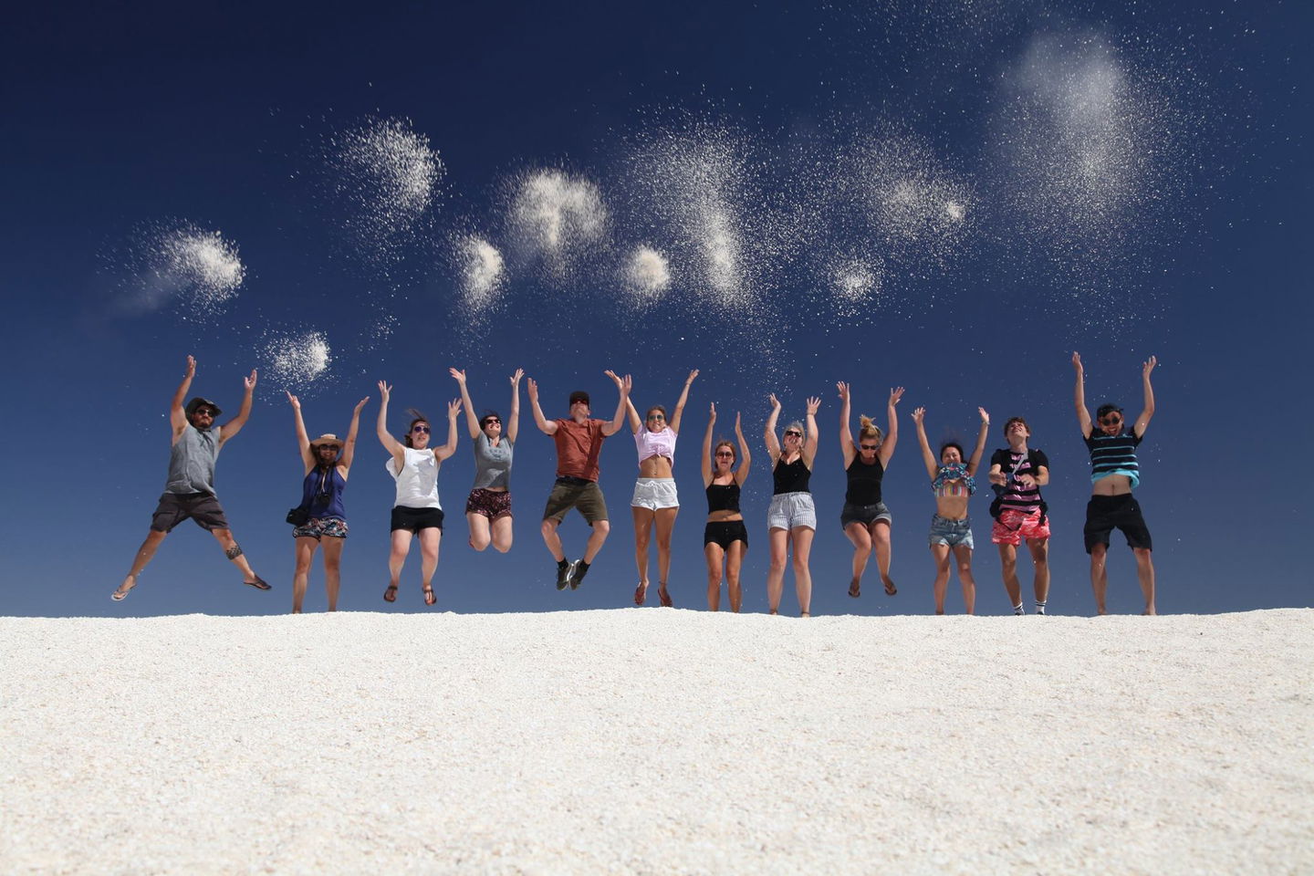 Group photo of travellers throwing sand in the air at Shell Beach