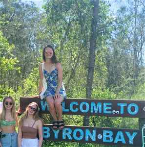 Group of travellers with a bike at 'Welcome to Byron Bay' Sign, Byron Bay, Australia