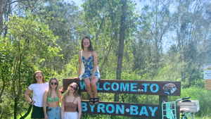 Group of travellers with a bike at 'Welcome to Byron Bay' Sign, Byron Bay, Australia