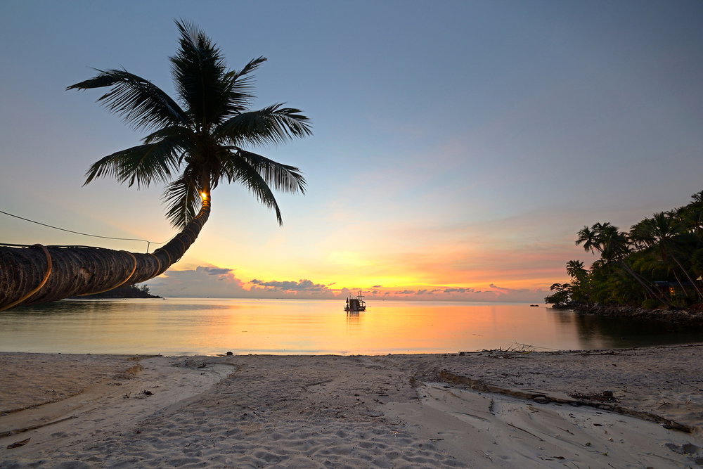 A lone boat sits in the water on a deserted beach at sunset