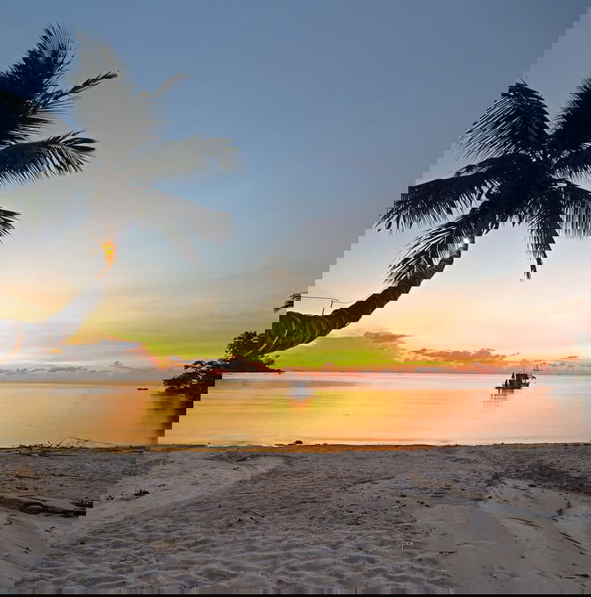 A lone boat sits in the water on a deserted beach at sunset