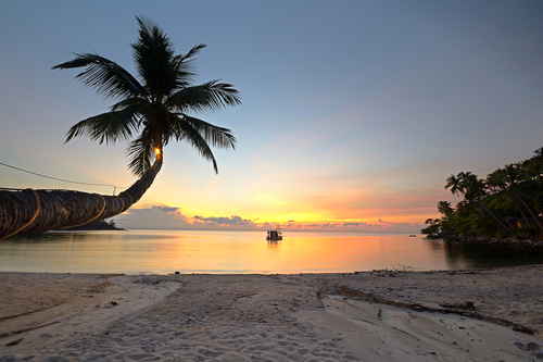A lone boat sits in the water on a deserted beach at sunset