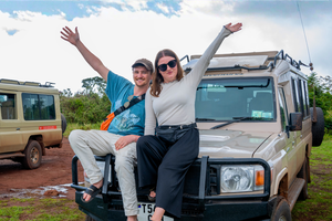 Two travellers on a group trip in Tanzania in front of a safari jeep