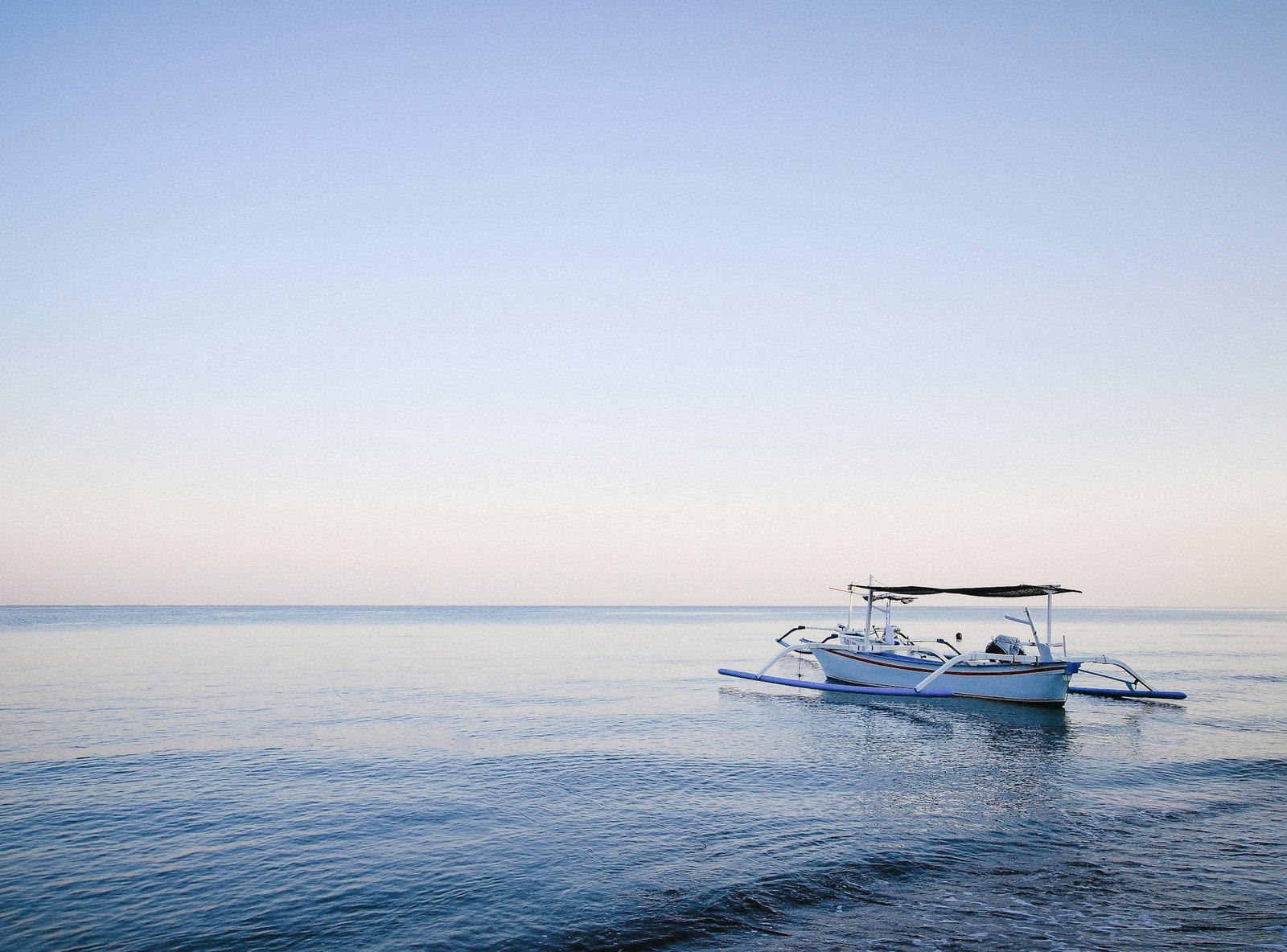 Traditional Balinese boat floating in blue ocean under baby blue skies, Lovina