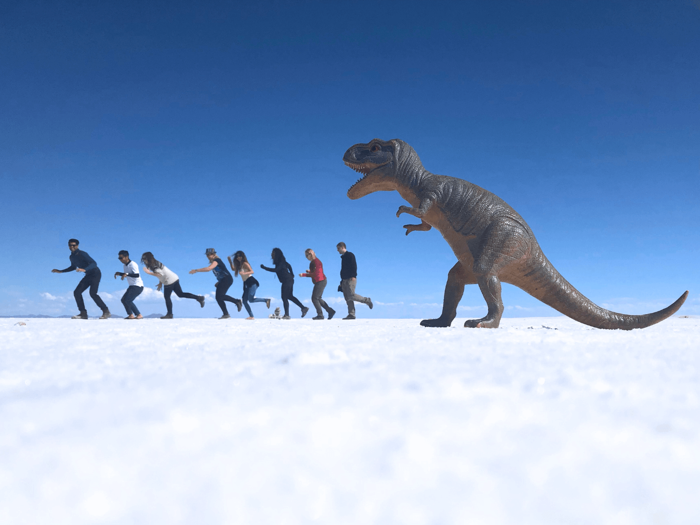Group travellers running from dinosaur toy in bolivia salt flat