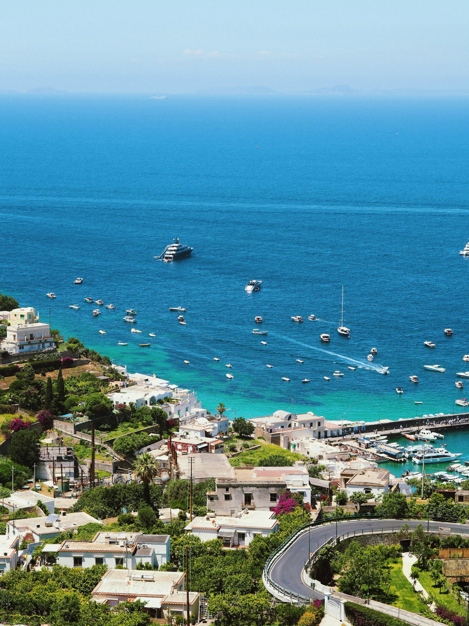 Road with traditional villages by a port filled with lots of sailboats on bright sapphire waters on a clear day