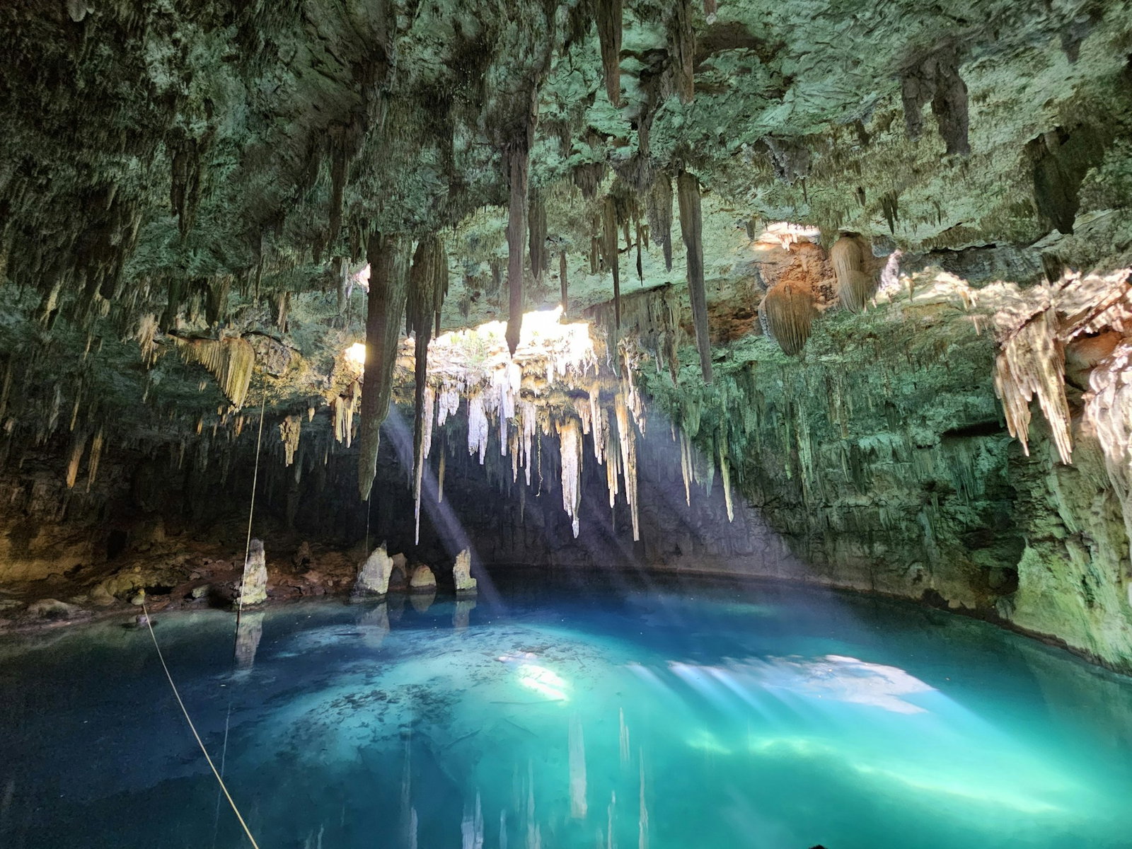 Cave with stalacites on the ceiling and a hole pouring sunlight onto the bright turquoise waters inside
