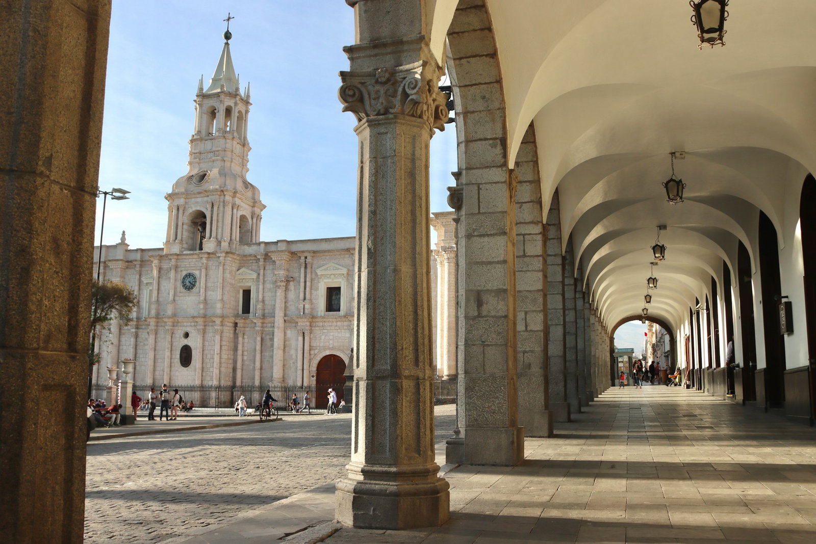 Traditional corridor with columns overlooking cobblestone street and classical white church with clear blue skies, Arequipa