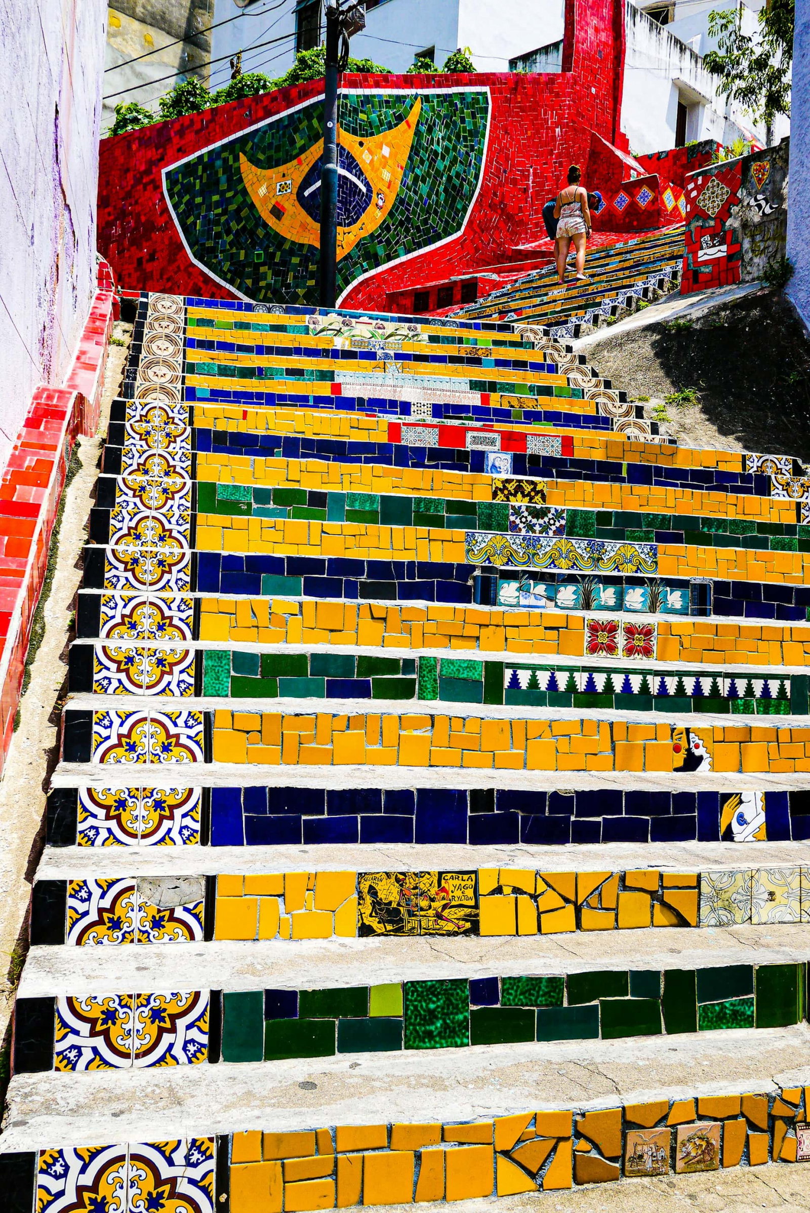 Colourful mosaic steps with Brazilian flag painted on mosaic red wall with person standing next to it