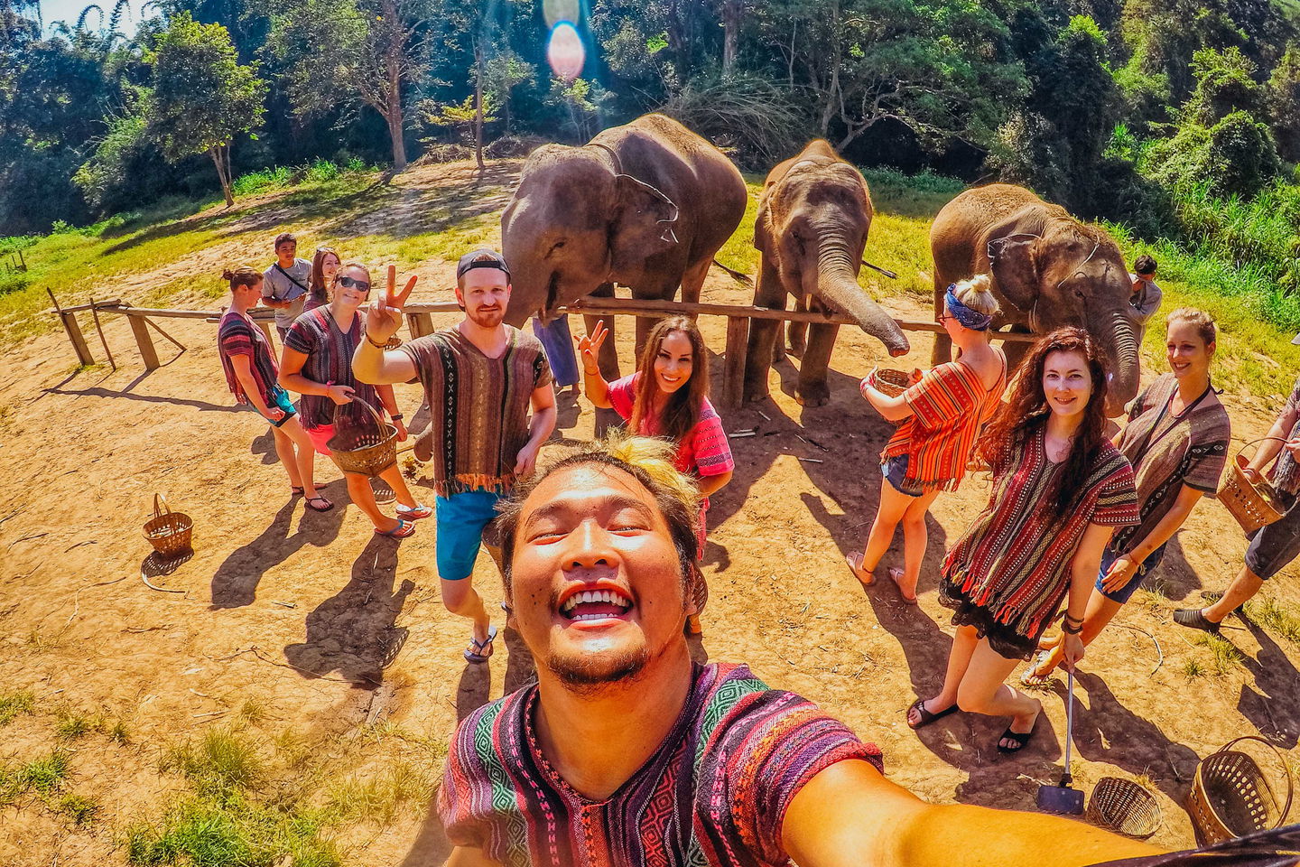 Group of young travellers taking selfie with elephants at sanctuary in Thailand