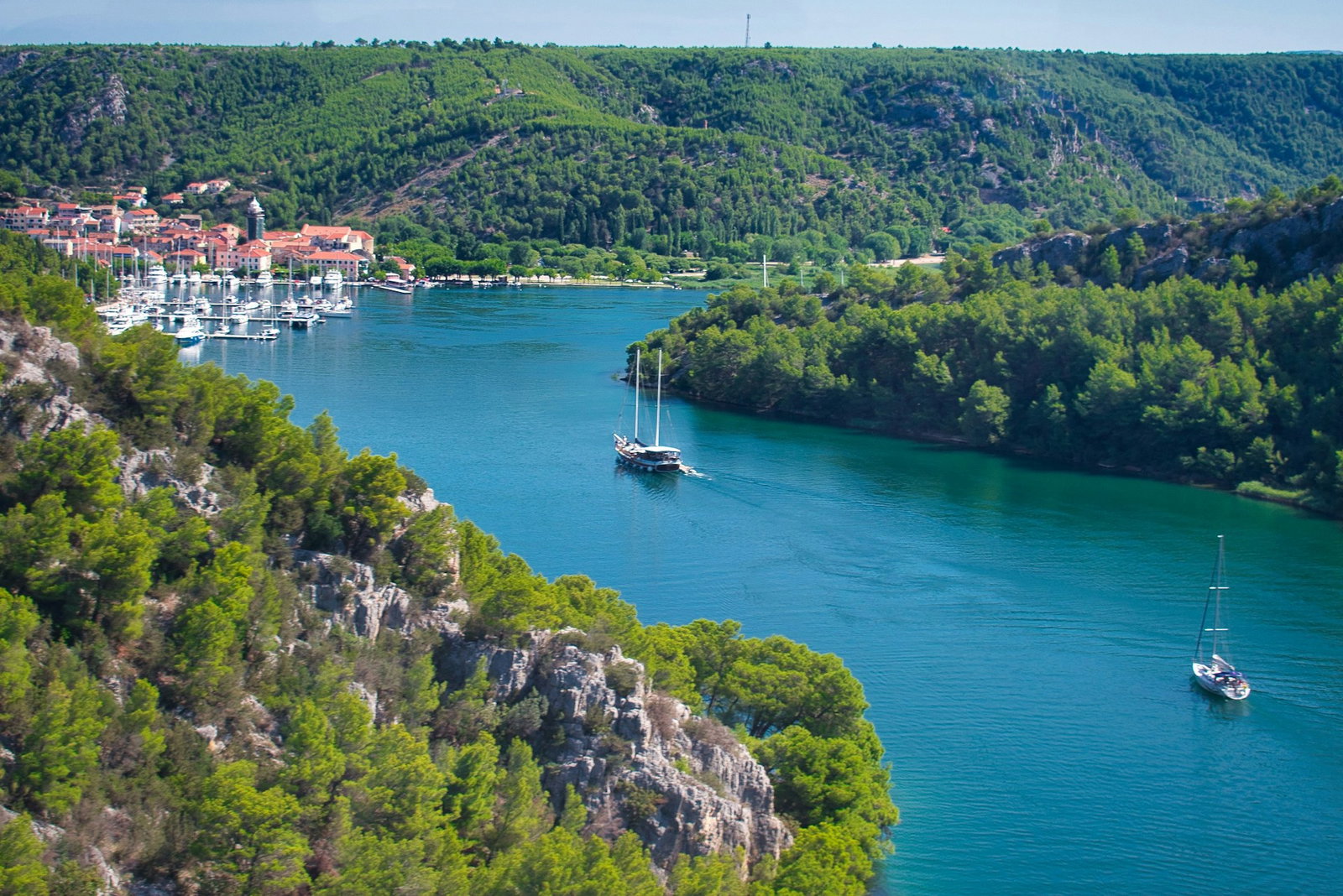 Modern sailboat gliding along deep turquoise waters surrounded by lush green hills and traditional Croatian port town