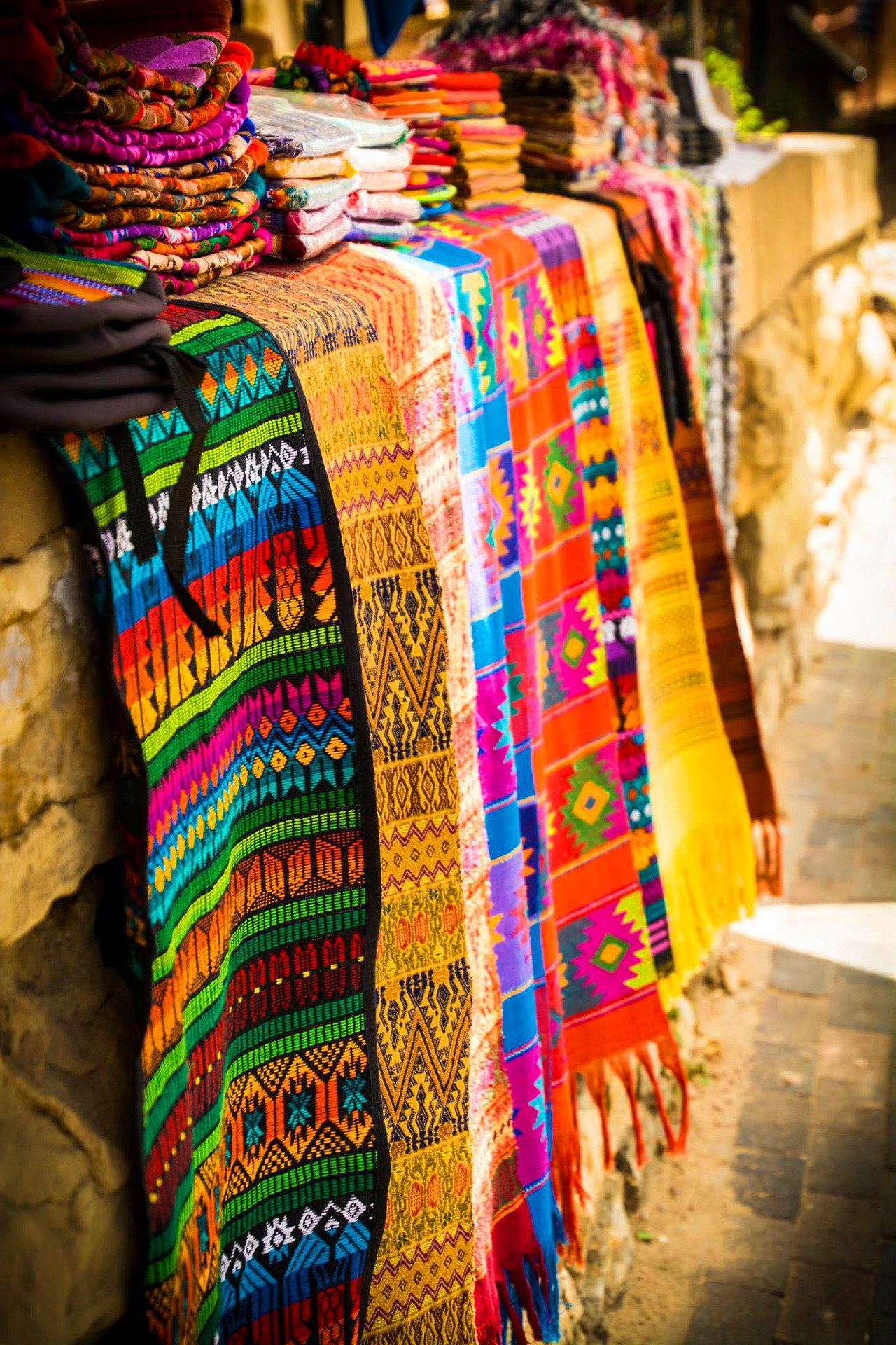 Traditional Native American fabrics hanging in organised pile on golden brown stone wall