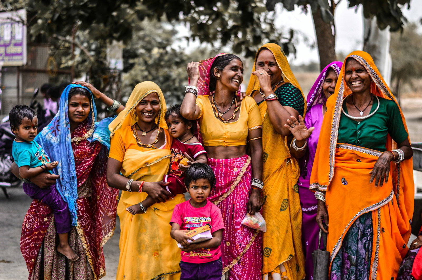 Group of women smiling and laughing while wearing traditional Indian clothing and carrying children