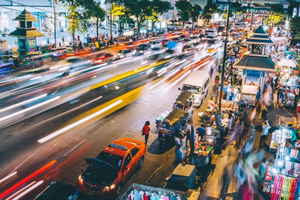Timelapse photo of a busy Bangkok street lined with Tuk Tuks and market stalls