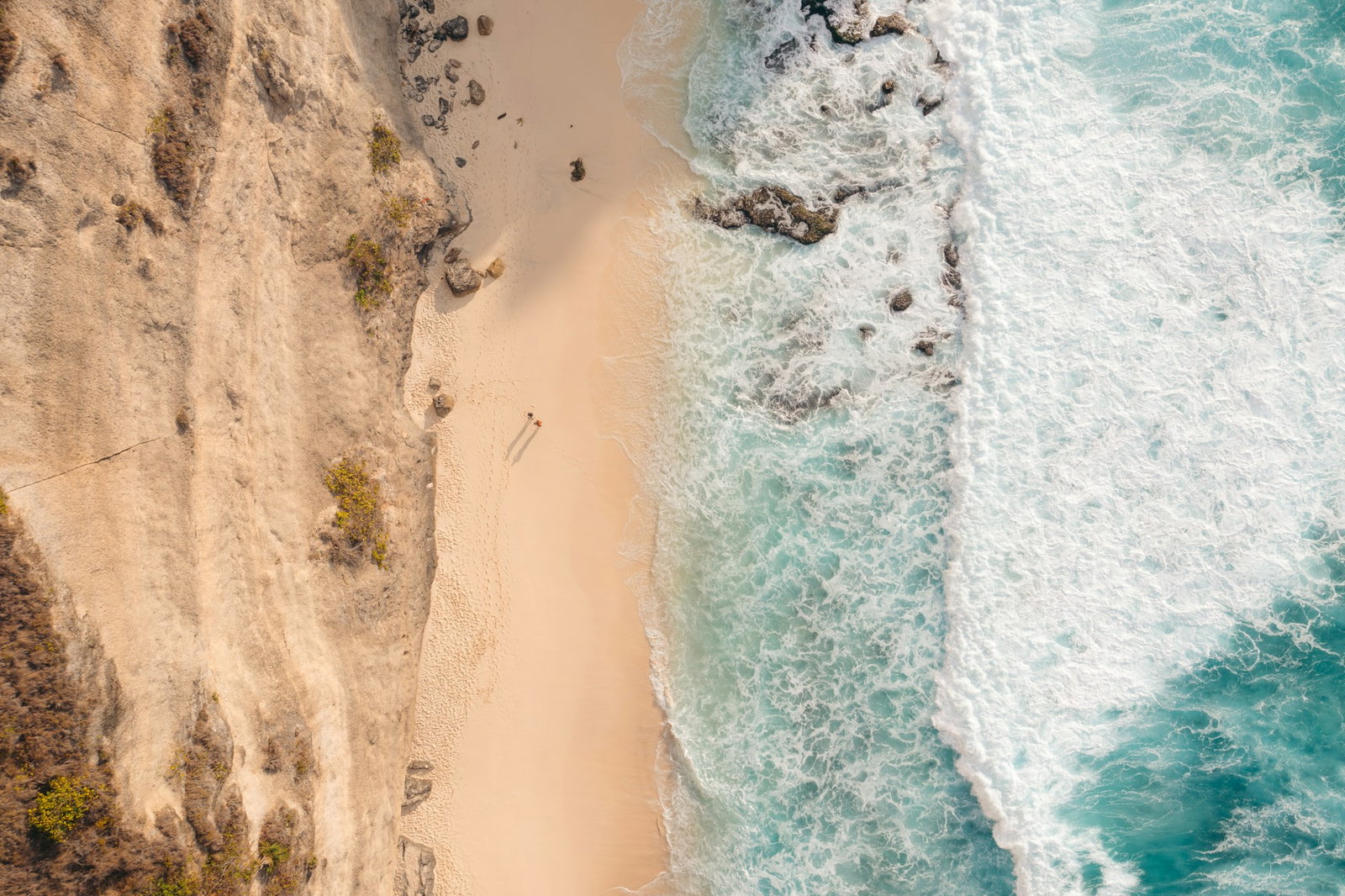 Aerial shot of golden sandy stretches backed by light brown cliffs and crashing waves from turquoise ocean, Nusa Penida