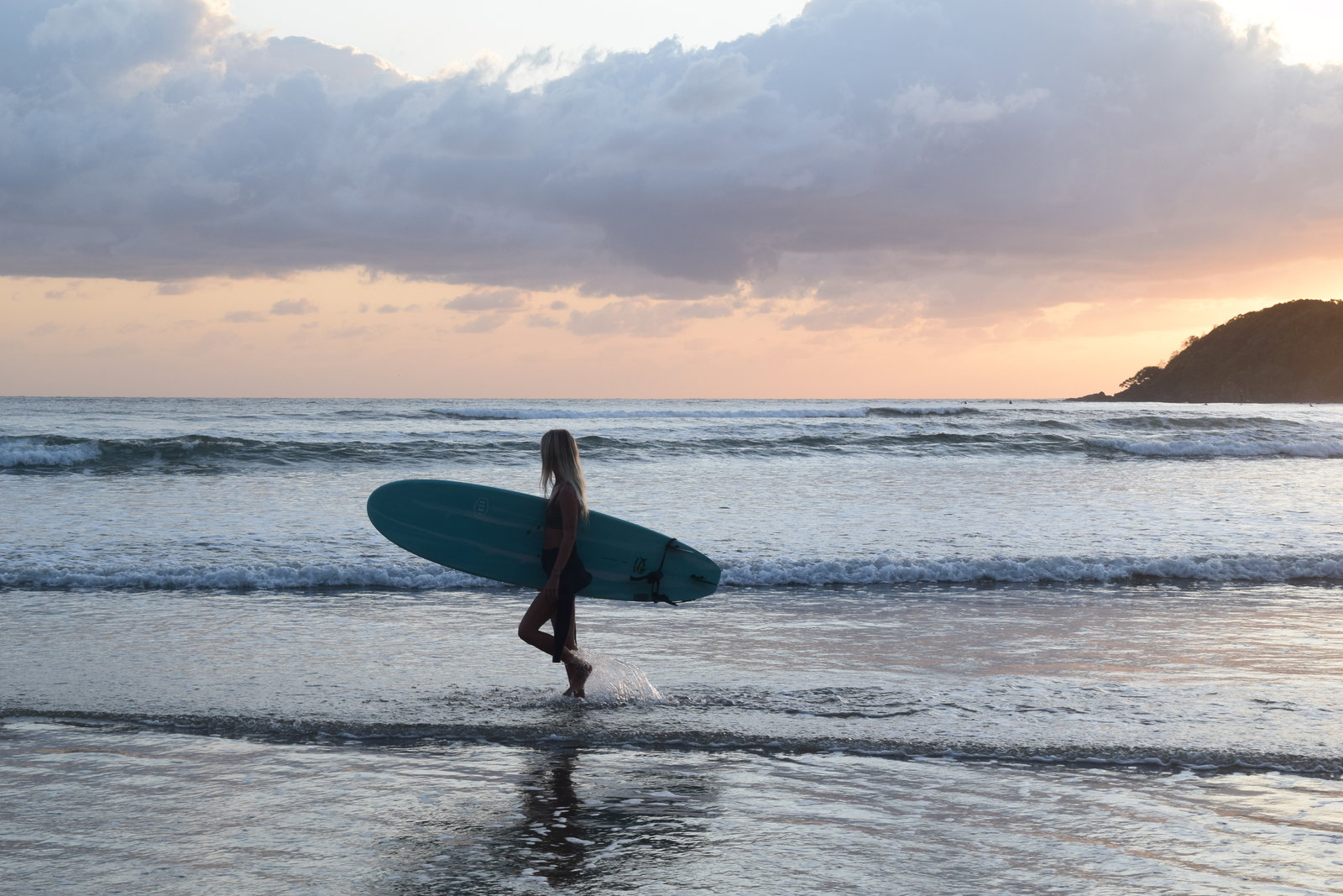 A traveller walks along a beach at sunset while waves crash at her feet