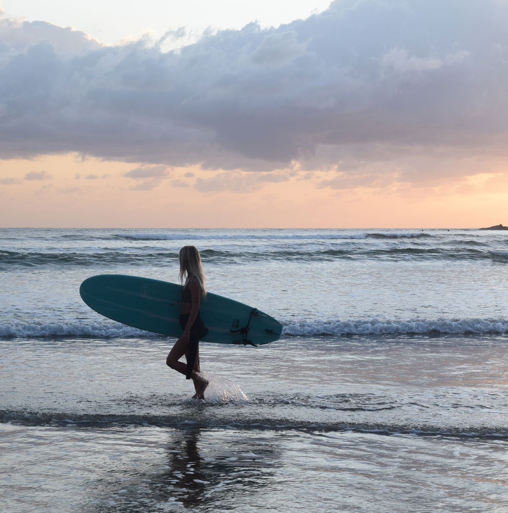 A traveller walks along a beach at sunset while waves crash at her feet