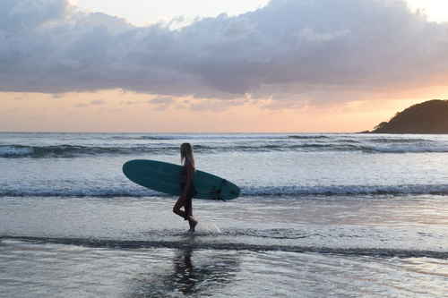 A traveller walks along a beach at sunset while waves crash at her feet
