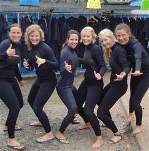 A group of travellers in wetsuits posing like they are surfing