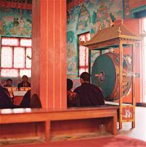 Buddhist monks in crimson robes sitting in a brightly coloured temple