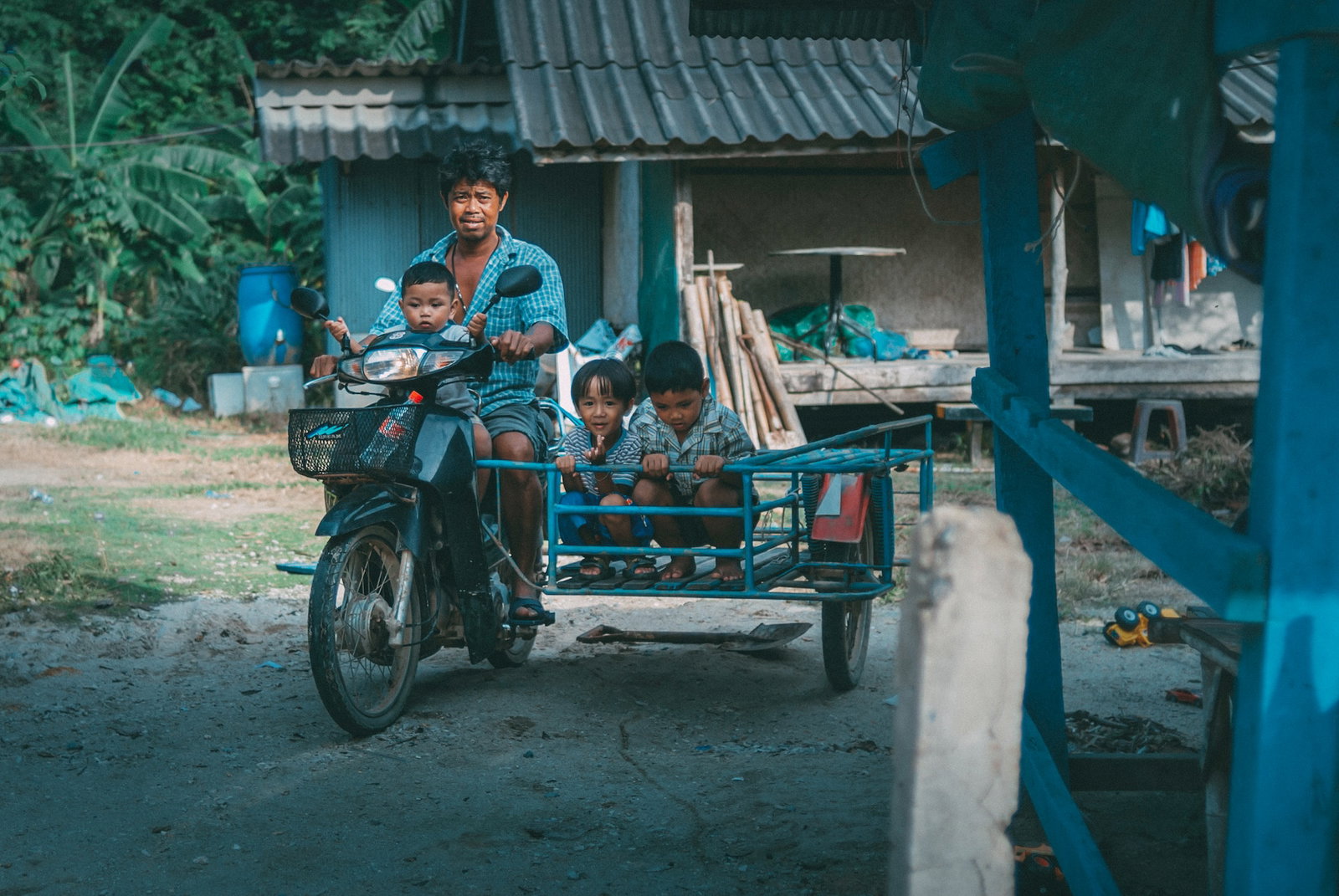 A Thai man rides a motorbike with a hand-built sidecar with kids riding in it