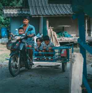 A Thai man rides a motorbike with a hand-built sidecar with kids riding in it