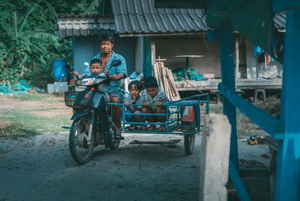 A Thai man rides a motorbike with a hand-built sidecar with kids riding in it