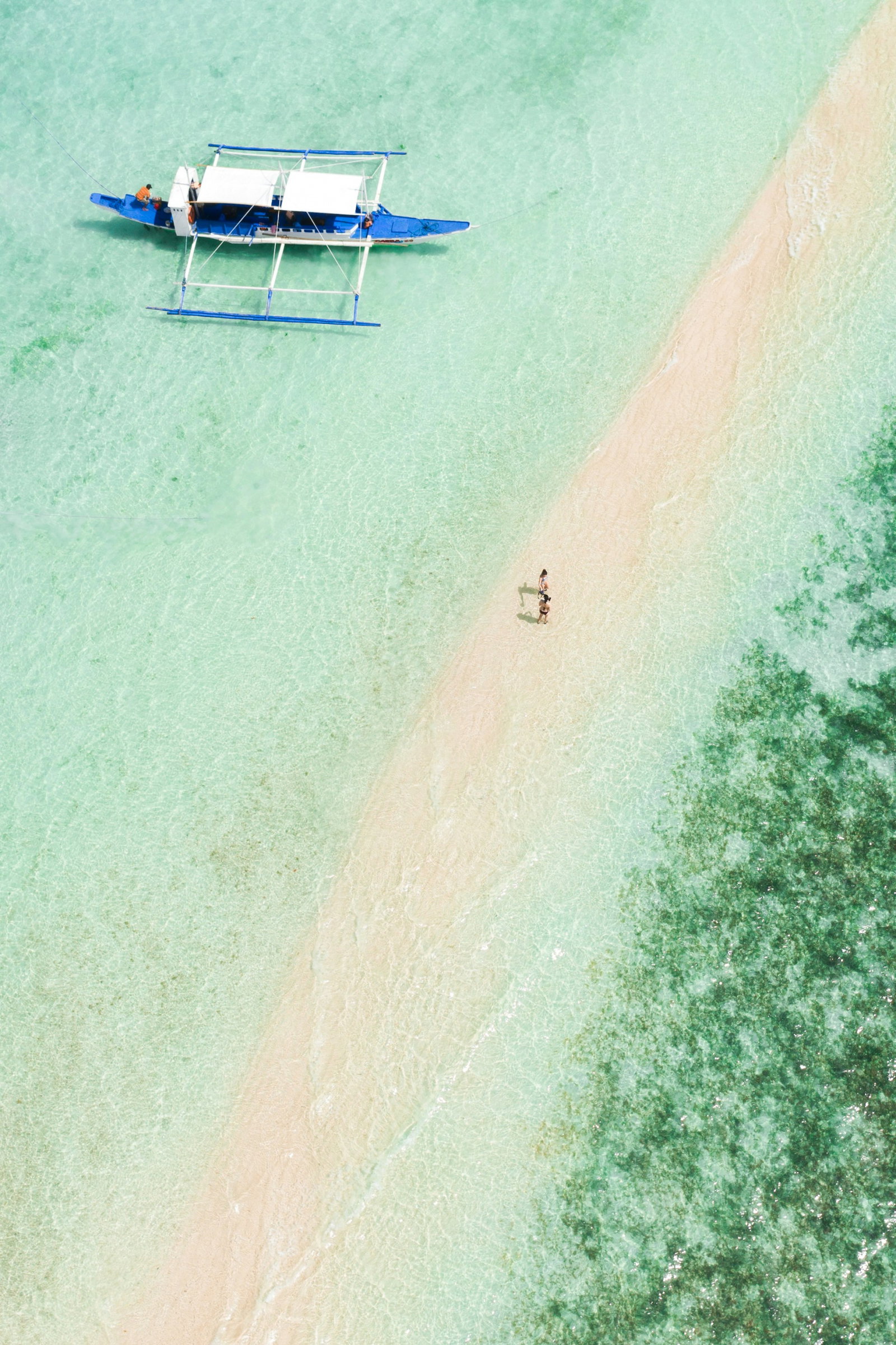 Aerial shot of little stretch of white sand and pastel aqua waters with traditional Filipino boat in the water, Philippines